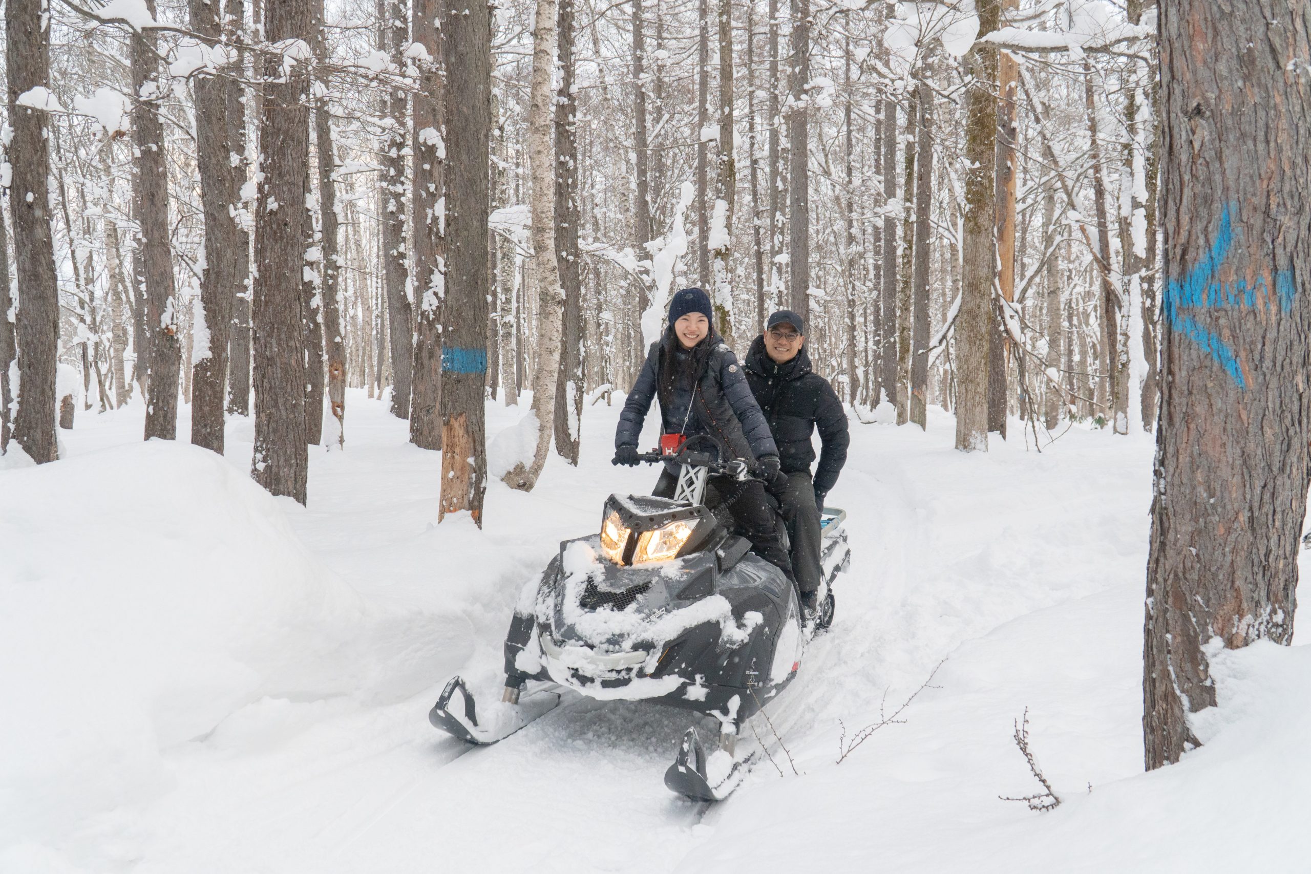 Guests riding a snowmobile through snow-covered forest near Niseko