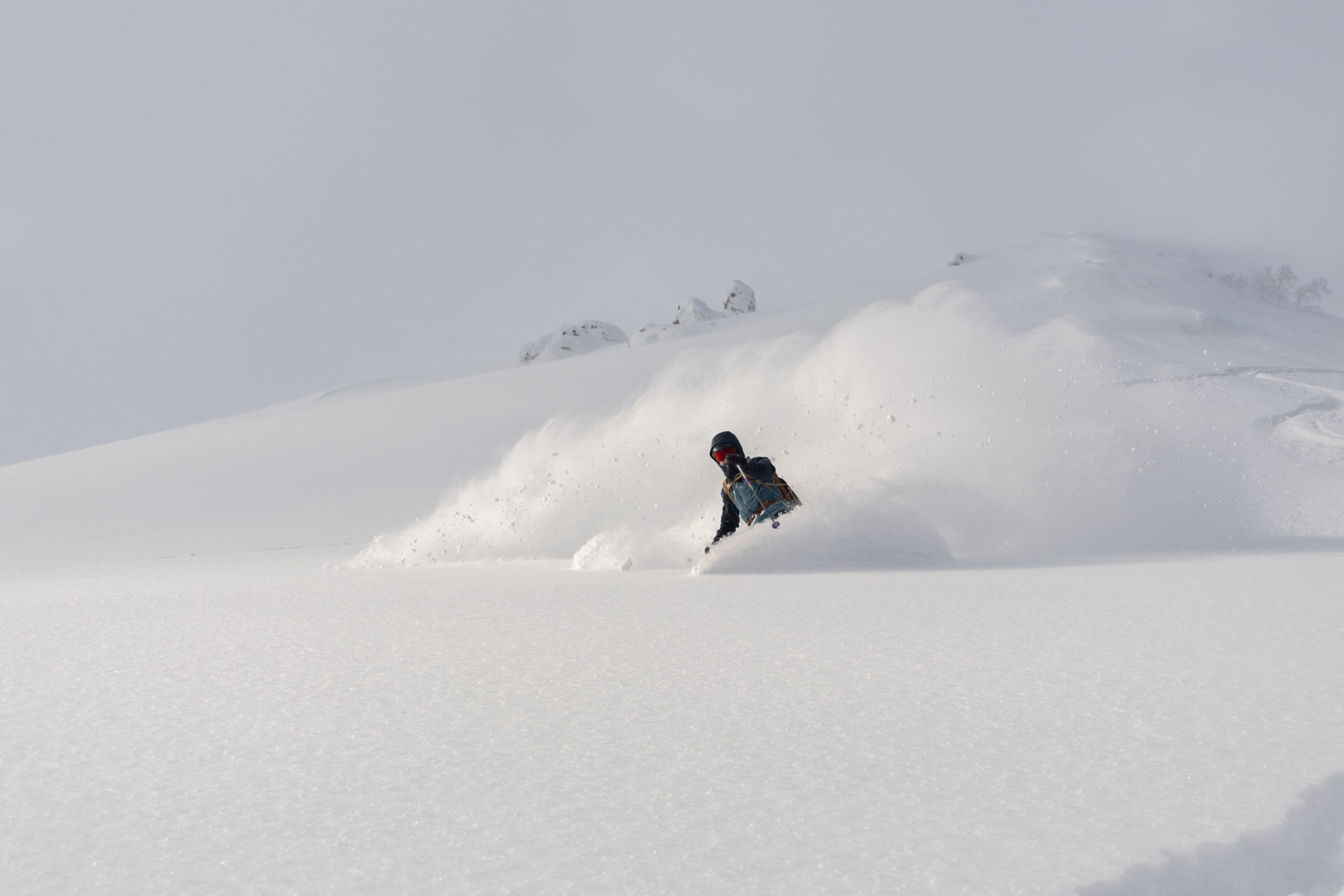 Skier sending snow into the air on a photographed Niseko backcountry tour