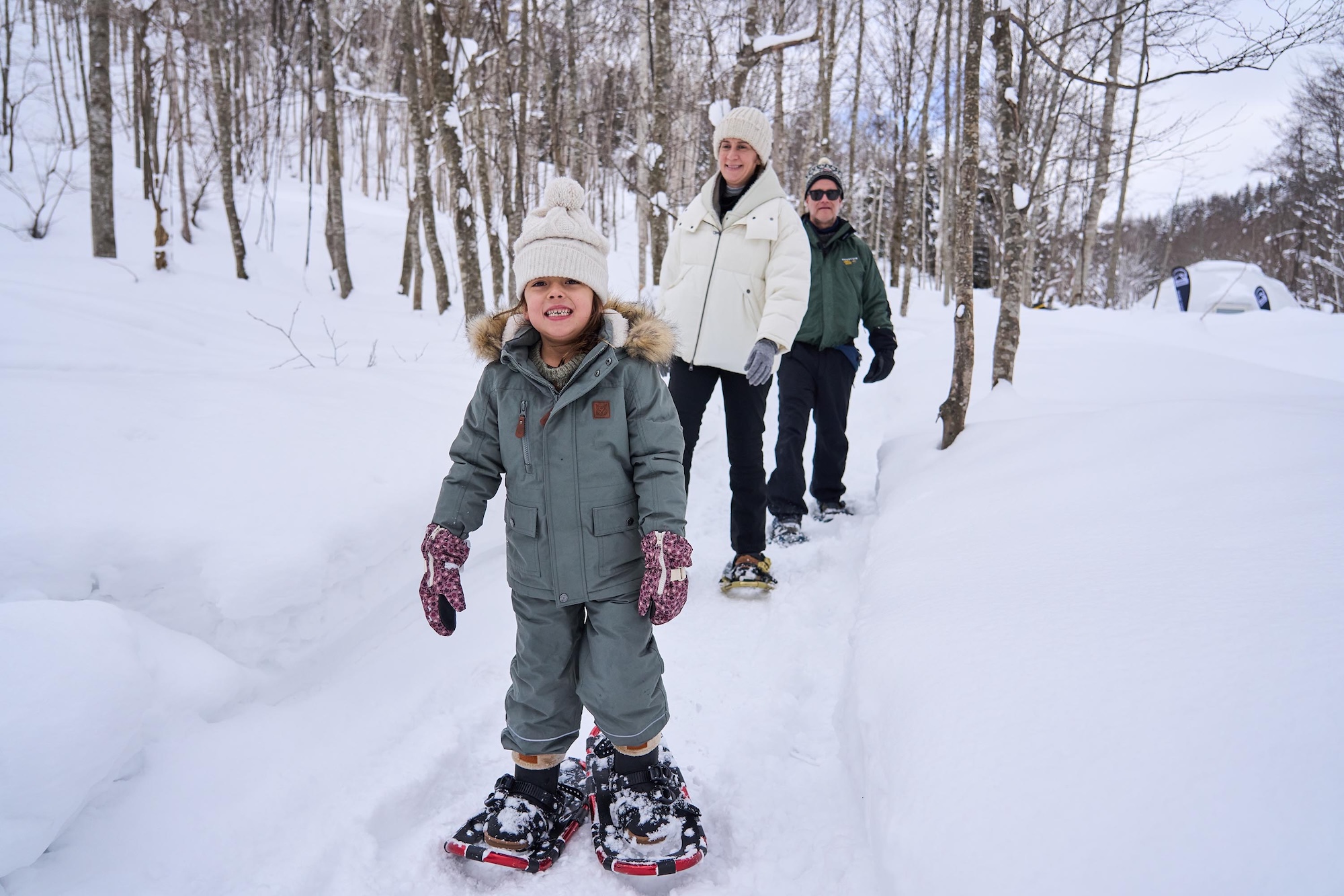 Child leading the family on snowshoes along a forest trail near Niseko