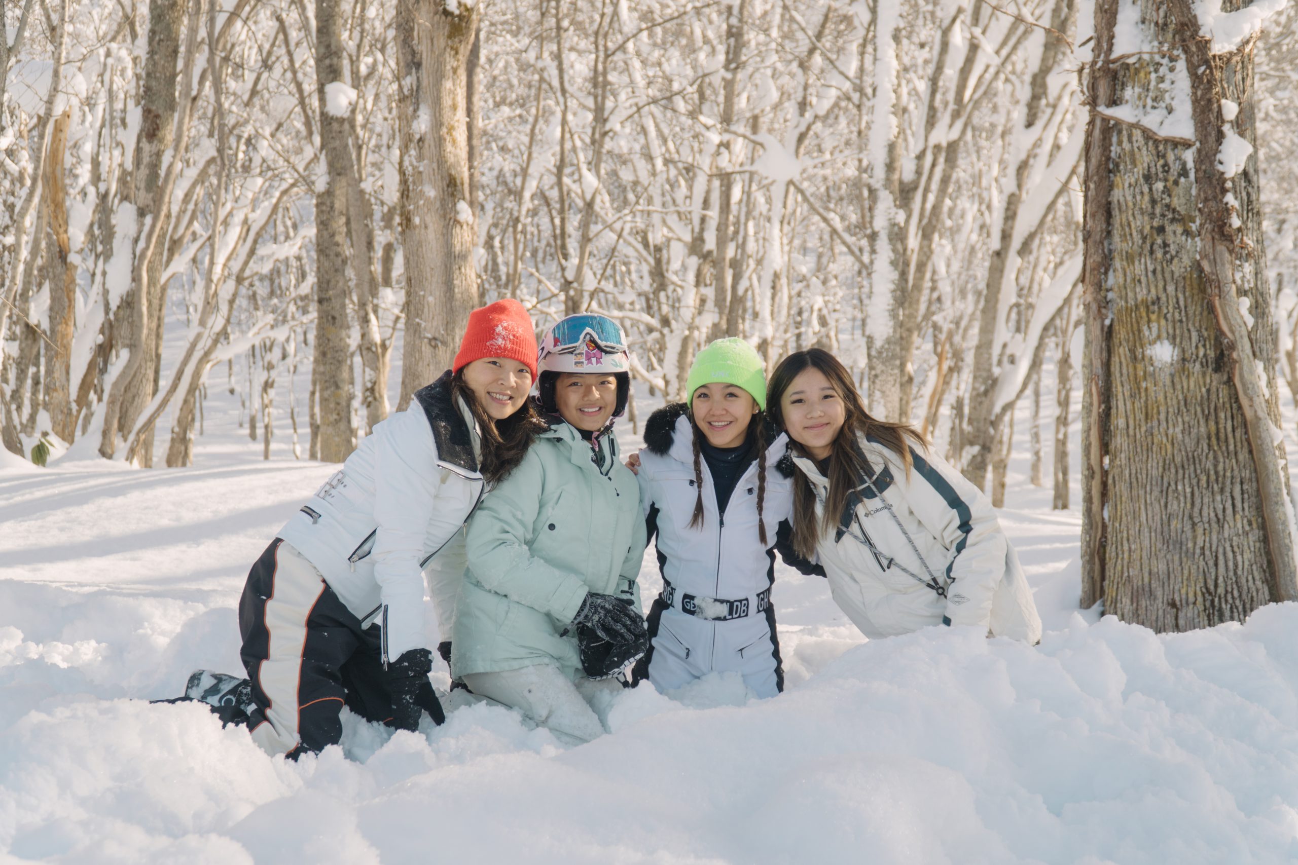 Family sitting together in deep snow among the birch trees in Niseko
