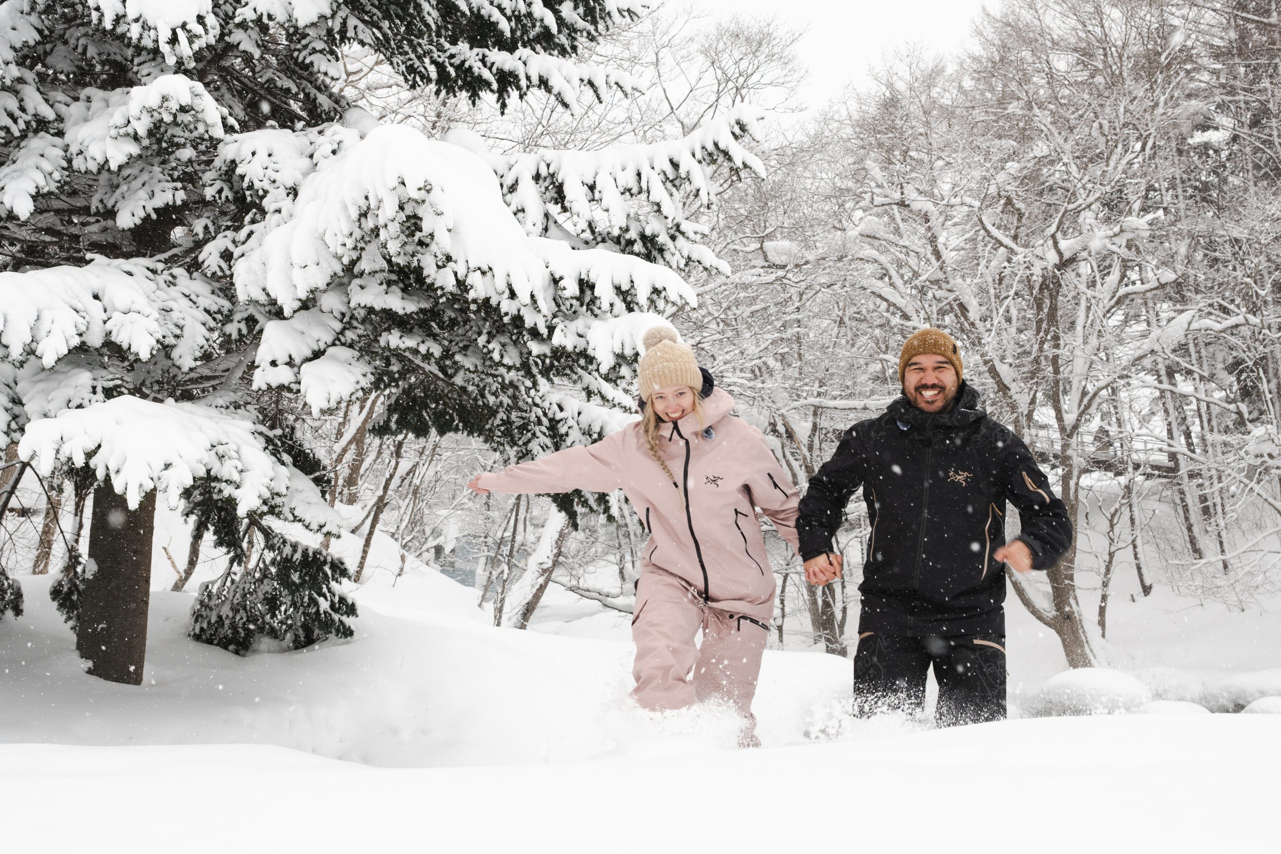 Couple running through deep powder snow in a Niseko forest during a snow portrait session