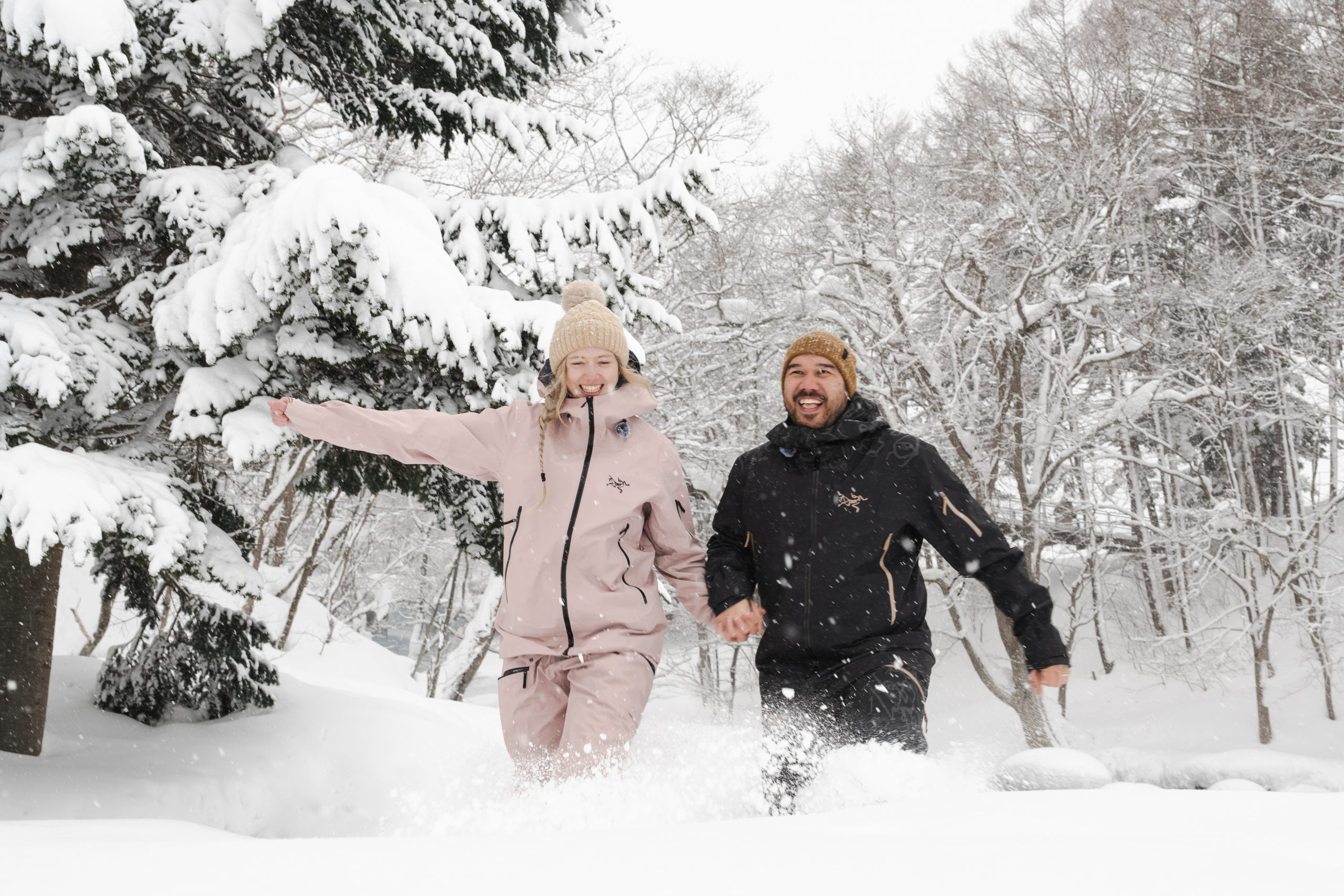 Couple running through deep powder in a snowy Niseko forest