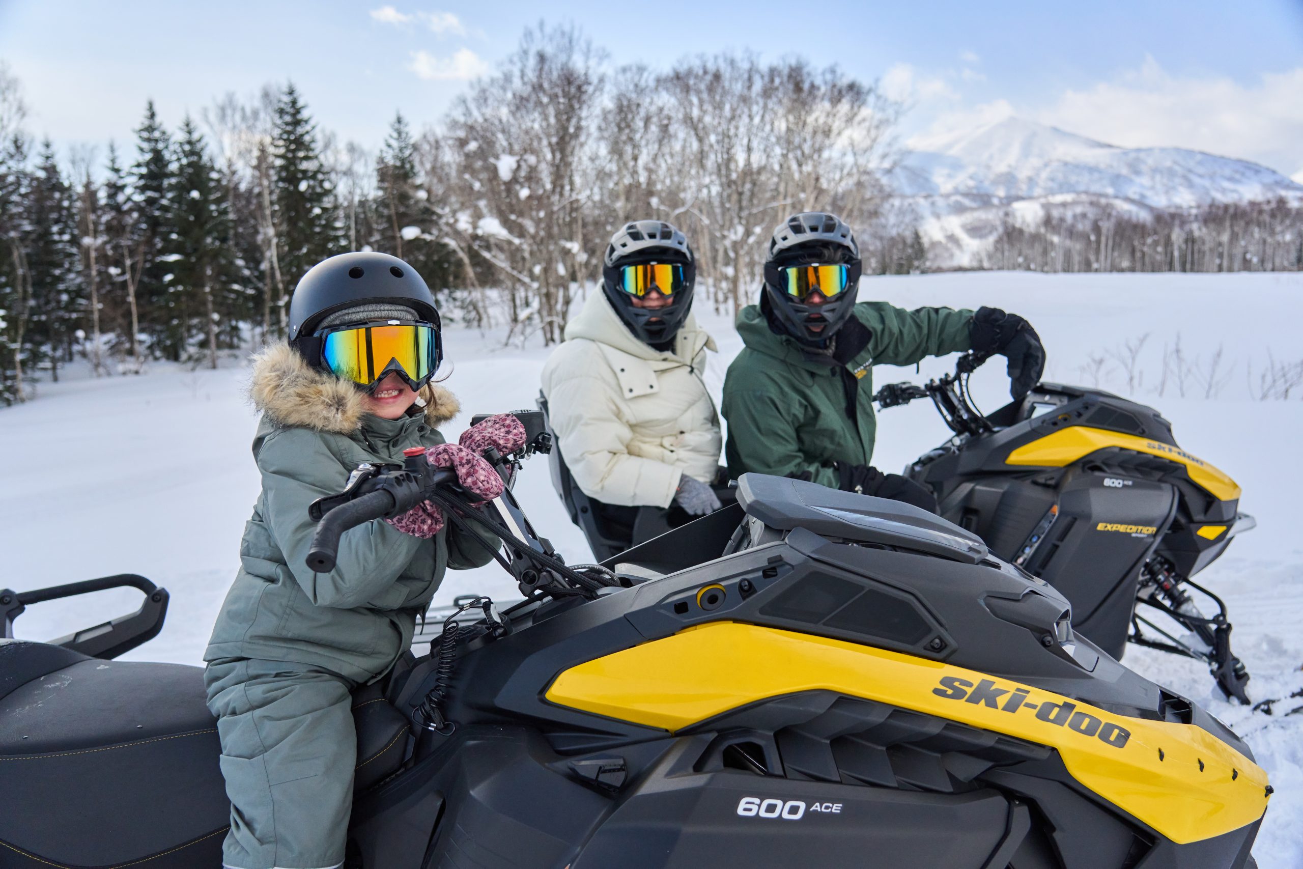 Family gearing up on snowmobiles under blue skies near Niseko