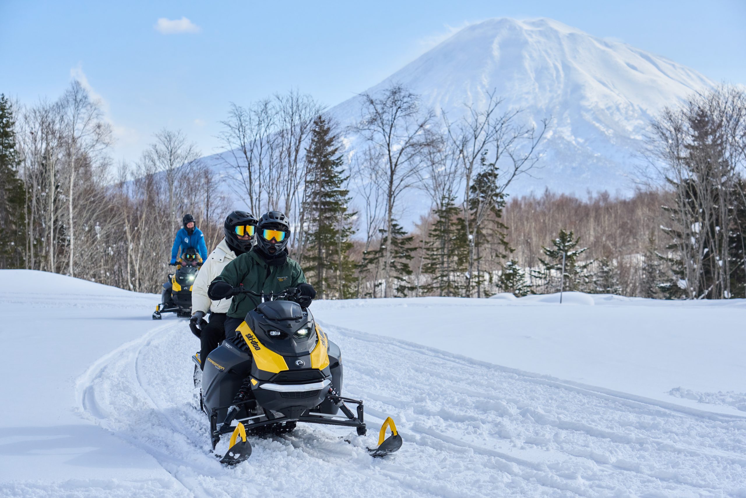 Snowmobile riders crossing fresh snow beneath Mt Yotei
