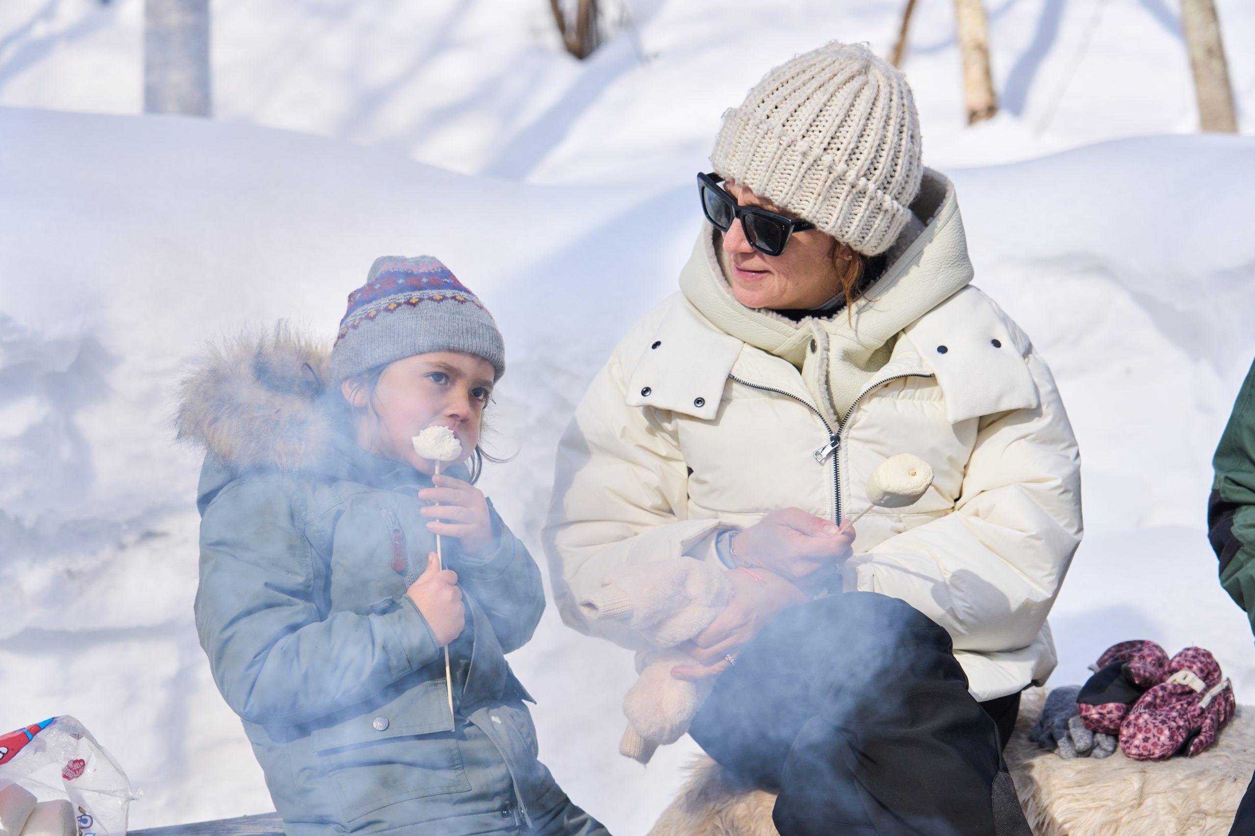 Child toasting a marshmallow by the campfire with her mother in the snow