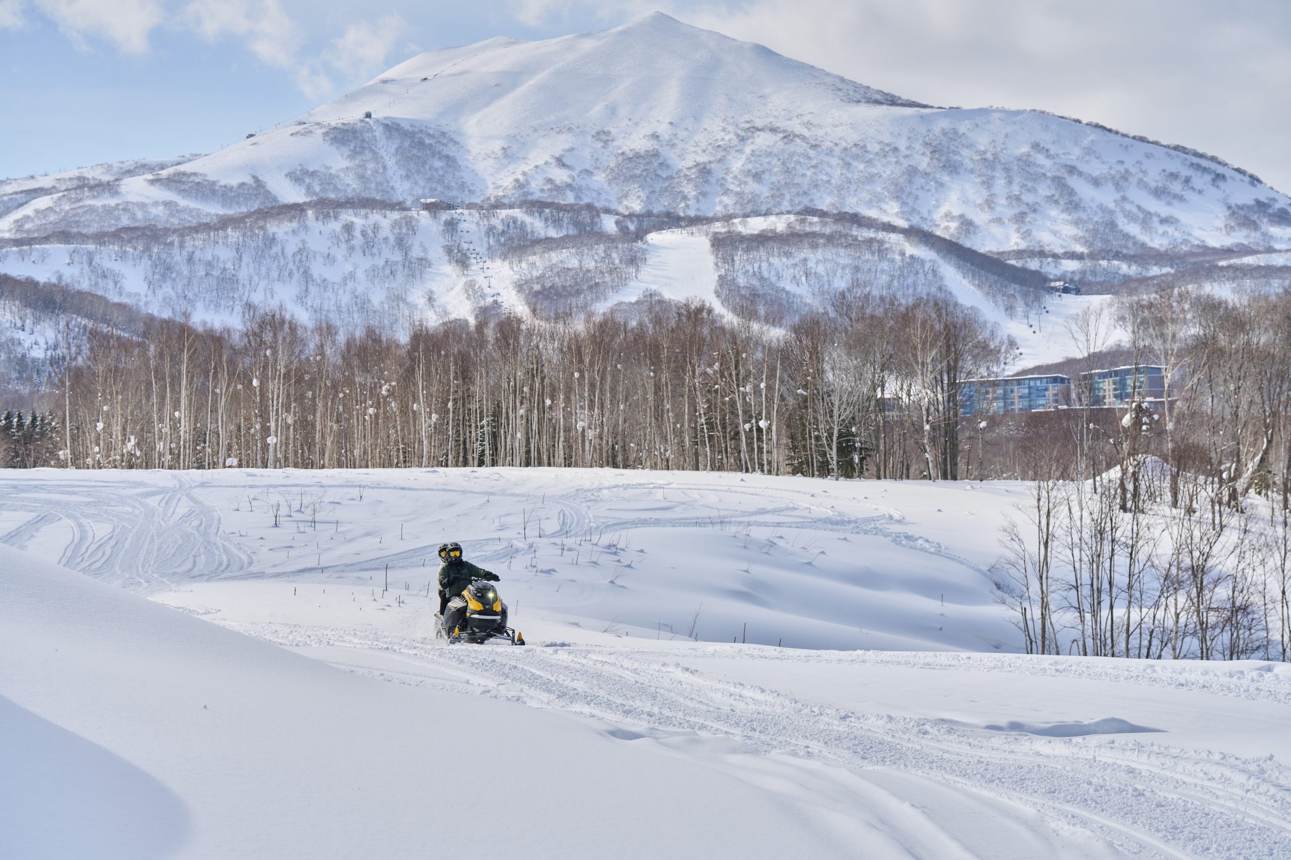 Snowmobile crossing wide open snowfields below the Niseko mountains