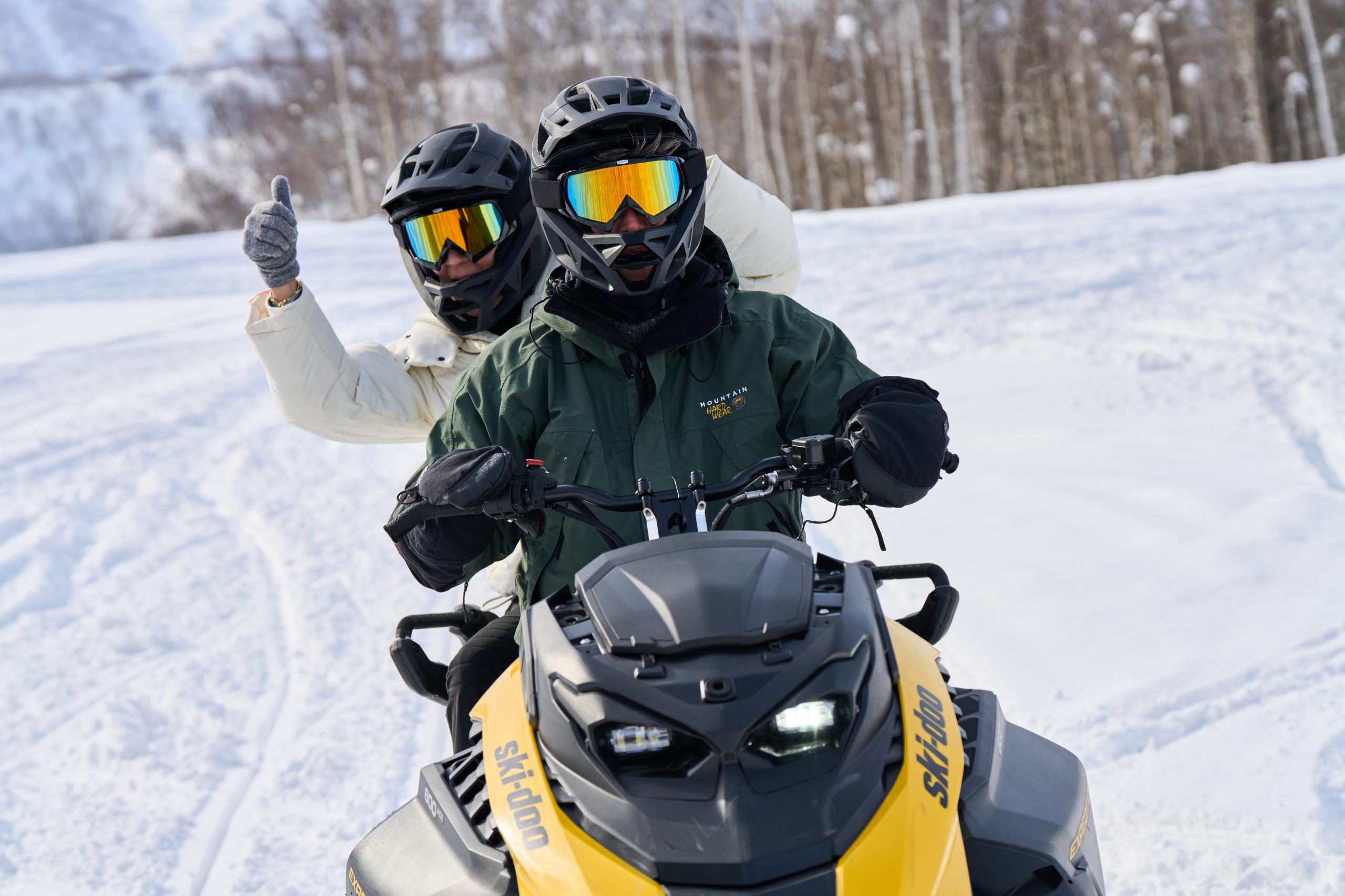Two guests giving a thumbs up from a snowmobile near Niseko