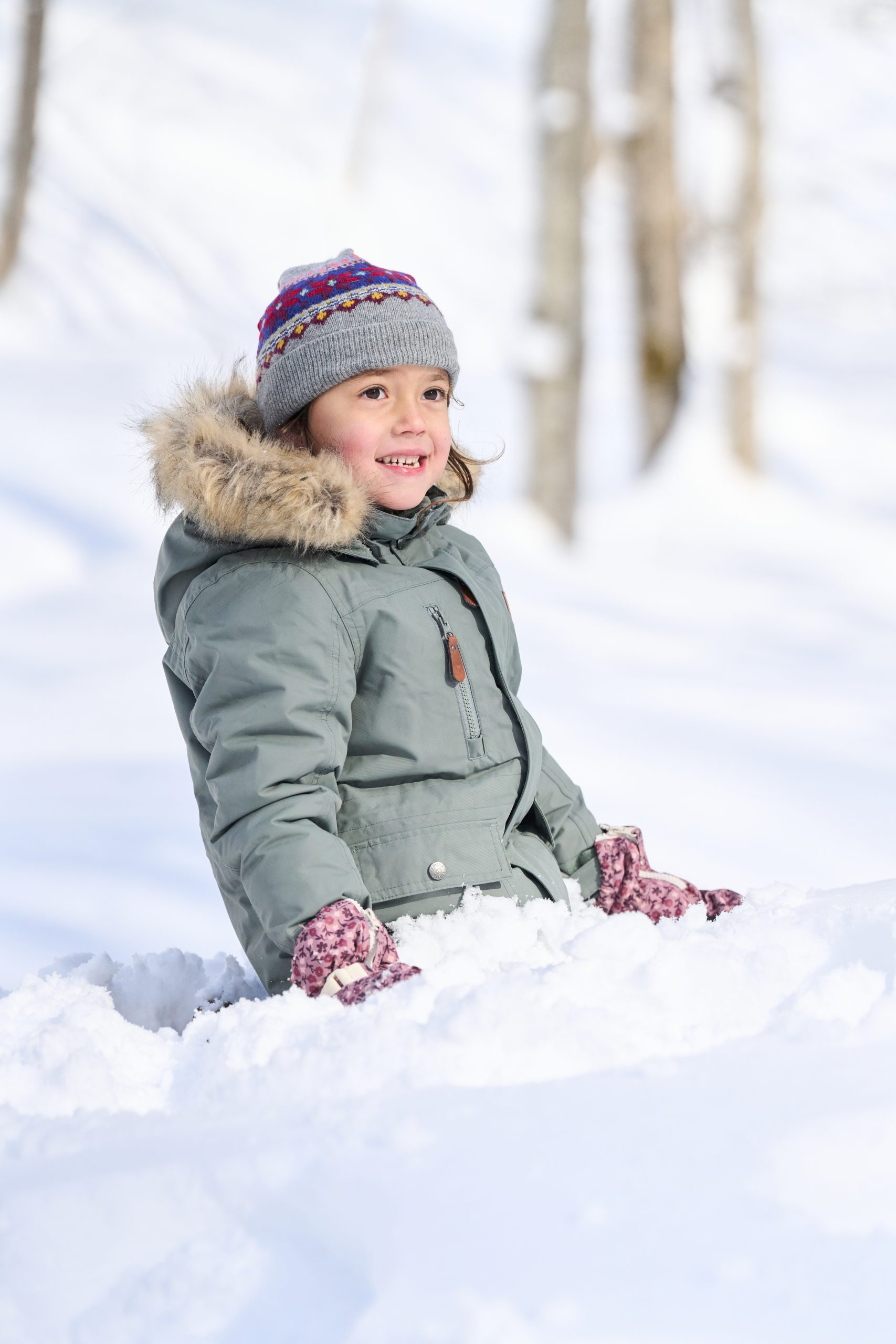 Laughing child sitting in deep snow in a Niseko forest