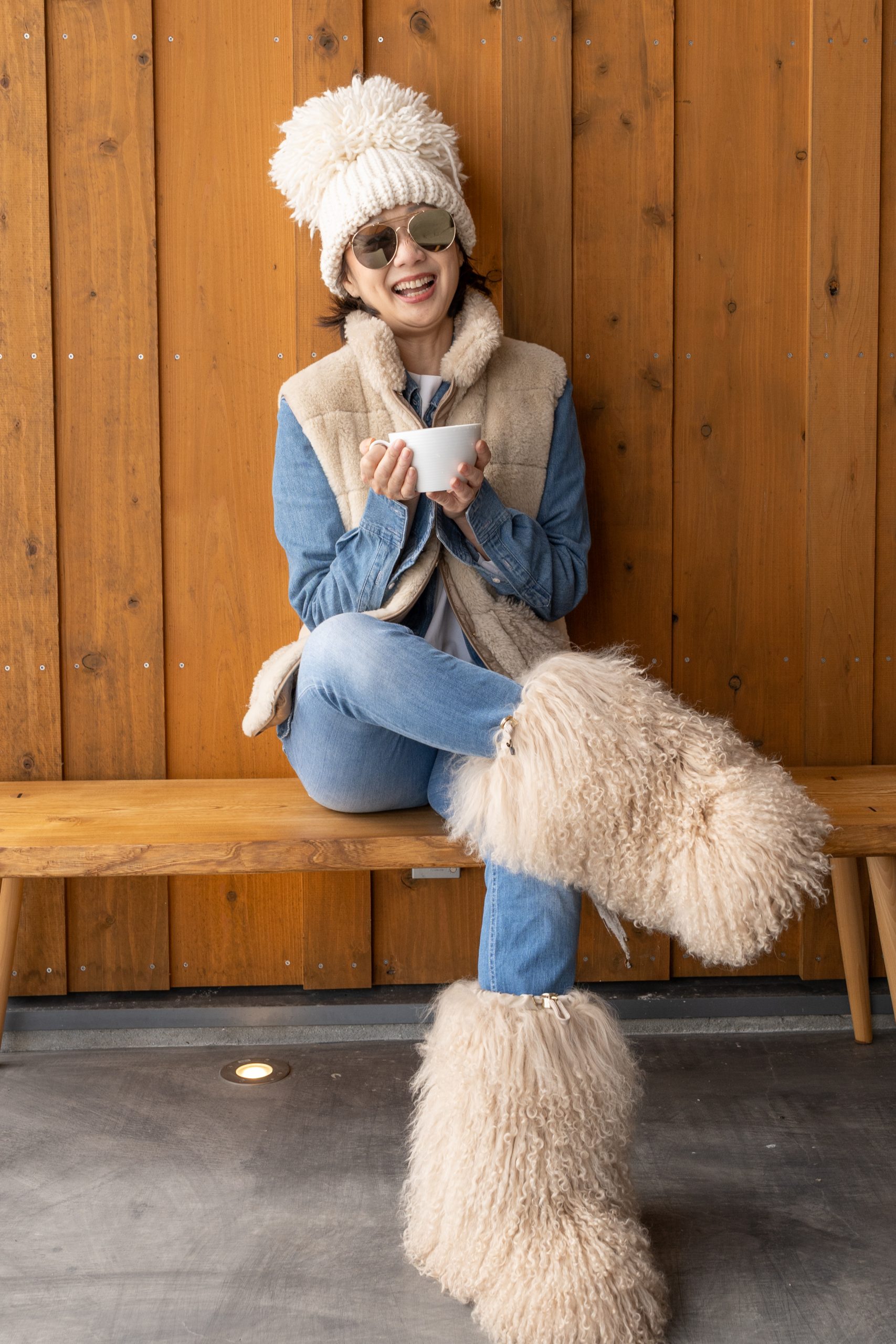 Woman in a knitted hat and wool boots smiling on a wooden bench in Niseko